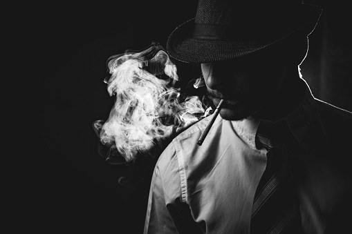 Retro-man-in-smoke-with-hat-shirt-and-tie-smoking-cigarette-black-and-white-Noir-style.jpg